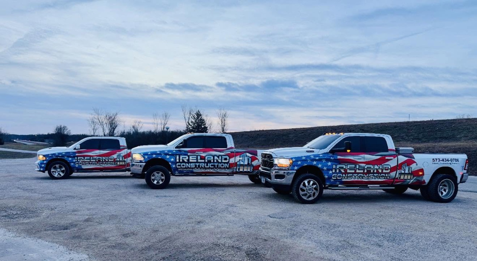 Three flag-wrapped Ireland Construction pickup trucks lined up at dusk