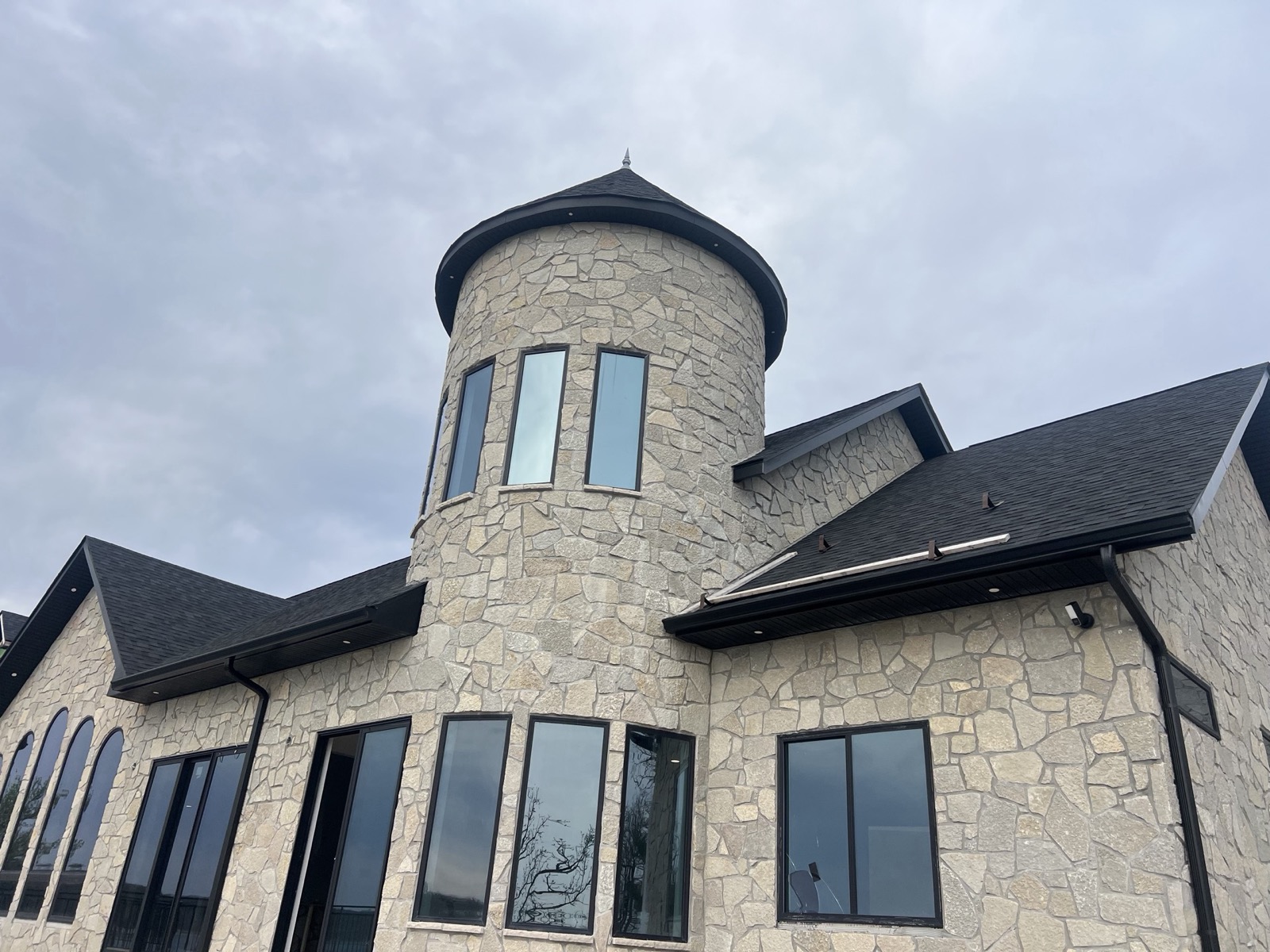 Custom stone home with a round turret, conical shingle roof, and tall black-framed windows, built by Ireland Construction