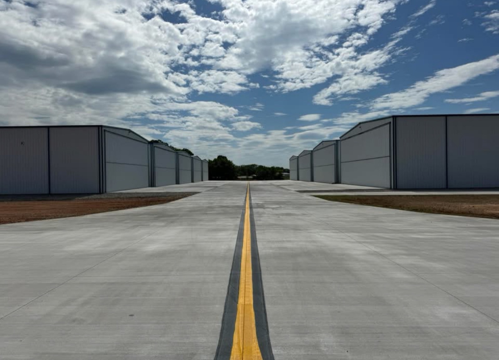 Rows of new white metal aircraft hangars along a fresh concrete taxiway, built by Ireland Construction