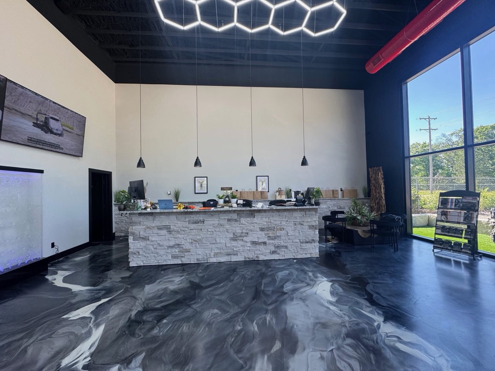 Commercial showroom lobby with a stacked-stone reception desk, hexagon LED lighting, and marbled epoxy floor finished by Ireland Construction