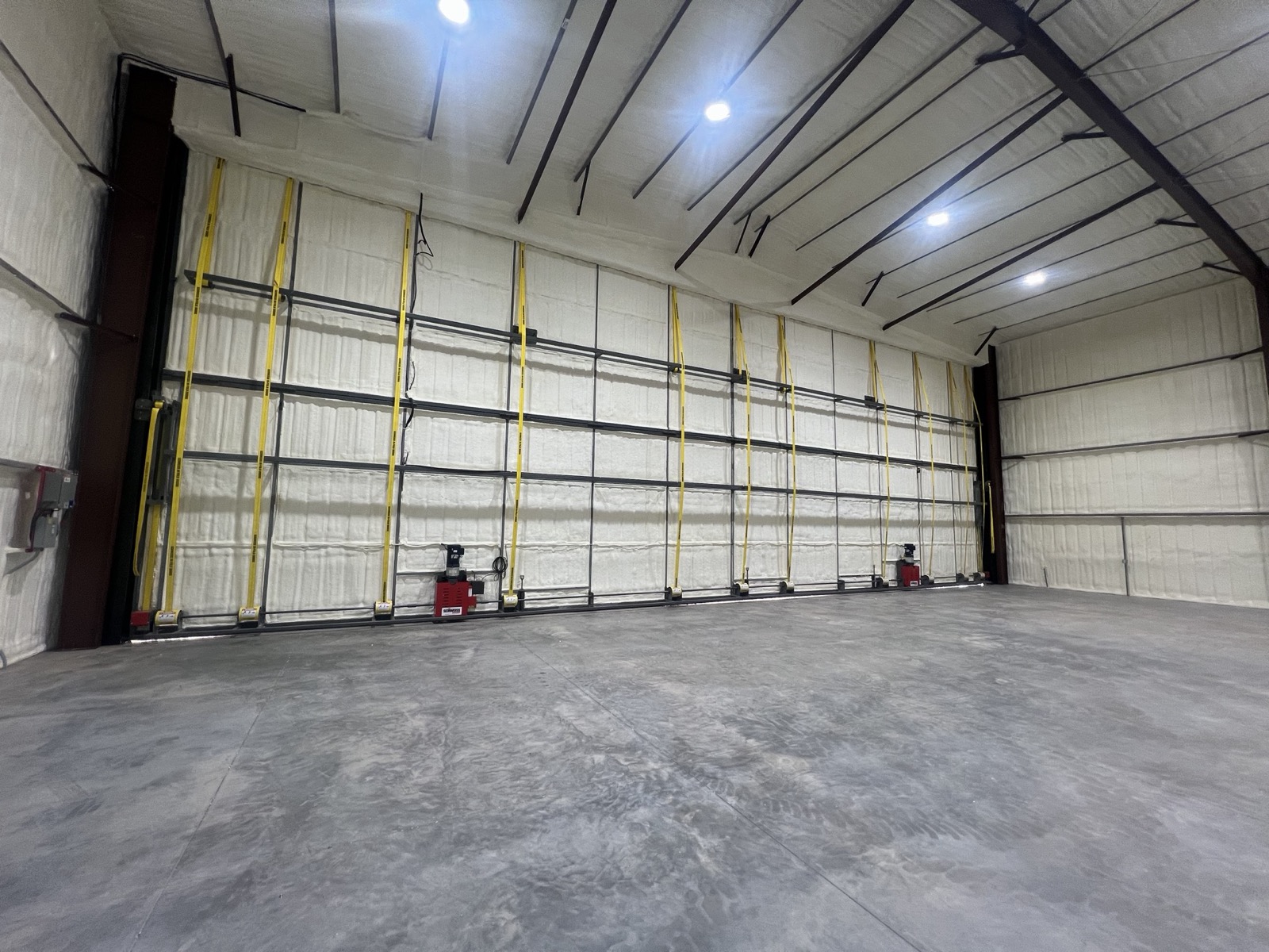 Bright hangar interior with spray-foam insulated walls, a full-width bifold door, and a finished concrete floor by Ireland Construction