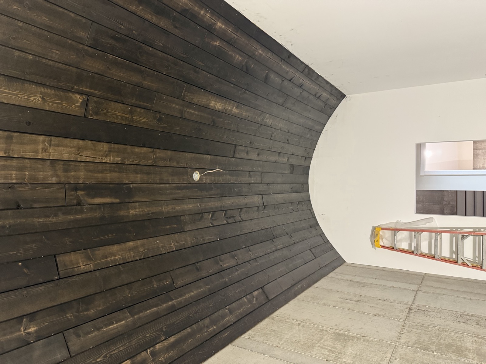 Curved accent wall of dark stained wood planks sweeping into a white ceiling, interior finish work by Ireland Construction