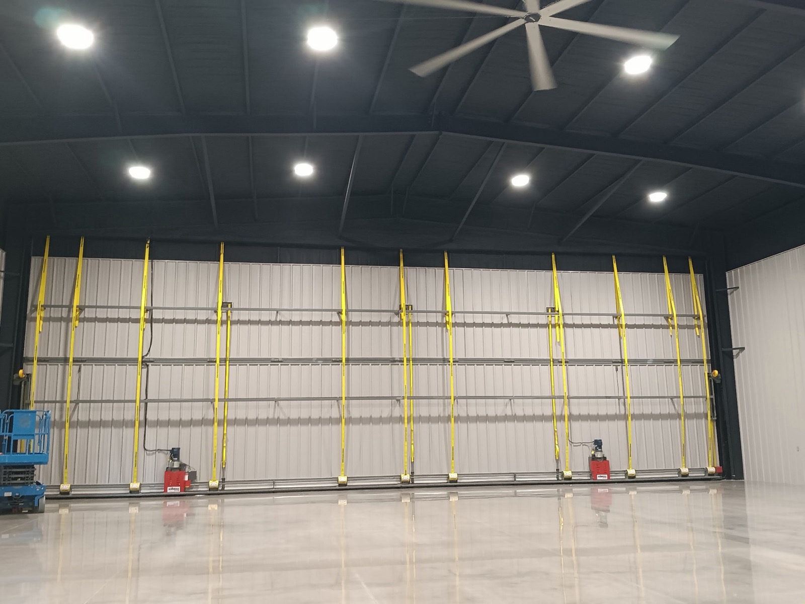 Steel hangar interior with a full-width hydraulic bifold door, industrial ceiling fan, and polished concrete floor built by Ireland Construction