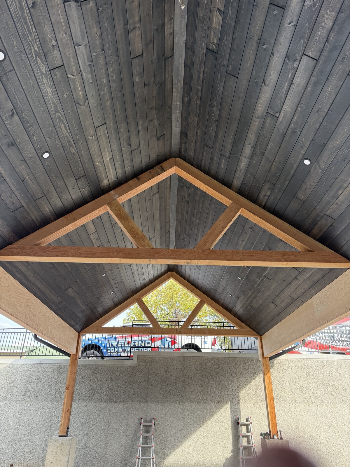 Dark-stained tongue-and-groove porch ceiling with an exposed king-post timber truss gable, craftsmanship by Ireland Construction