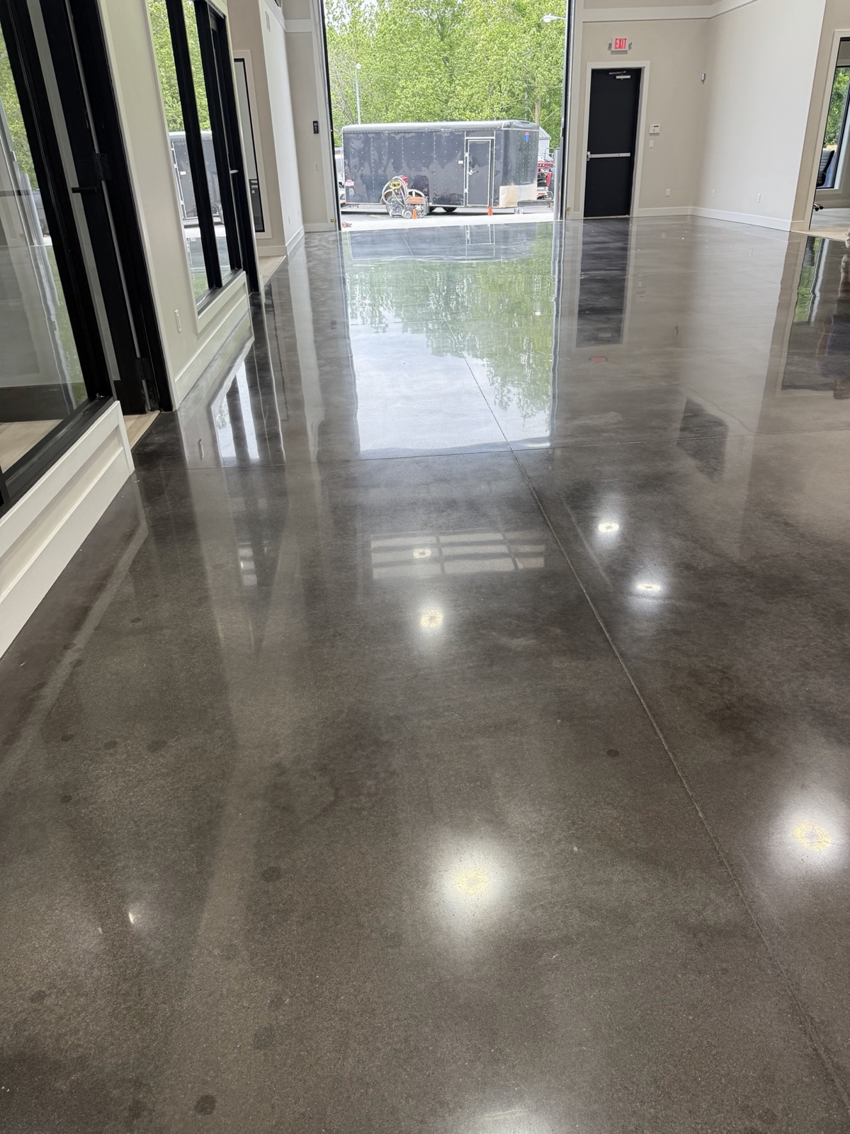 Freshly polished concrete floor with a mirror sheen reflecting recessed lights and black-framed windows, concrete work by Ireland Construction