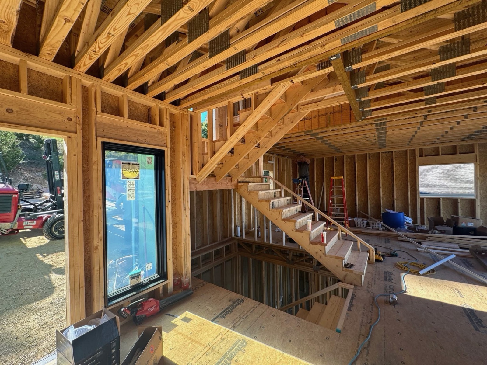 Interior framing of a custom home with a new wood staircase and exposed trusses in warm sunlight on an Ireland Construction jobsite
