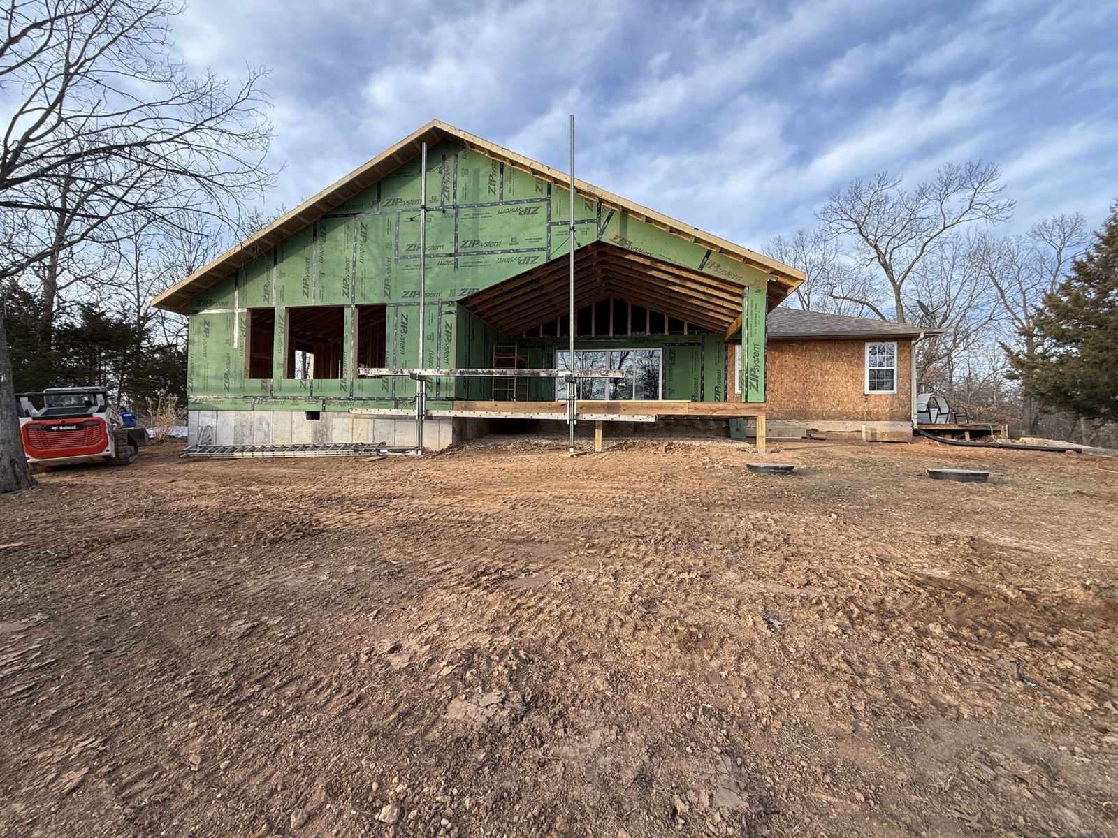 Home addition wrapped in weather sheathing with a vaulted timber porch roof under construction by Ireland Construction