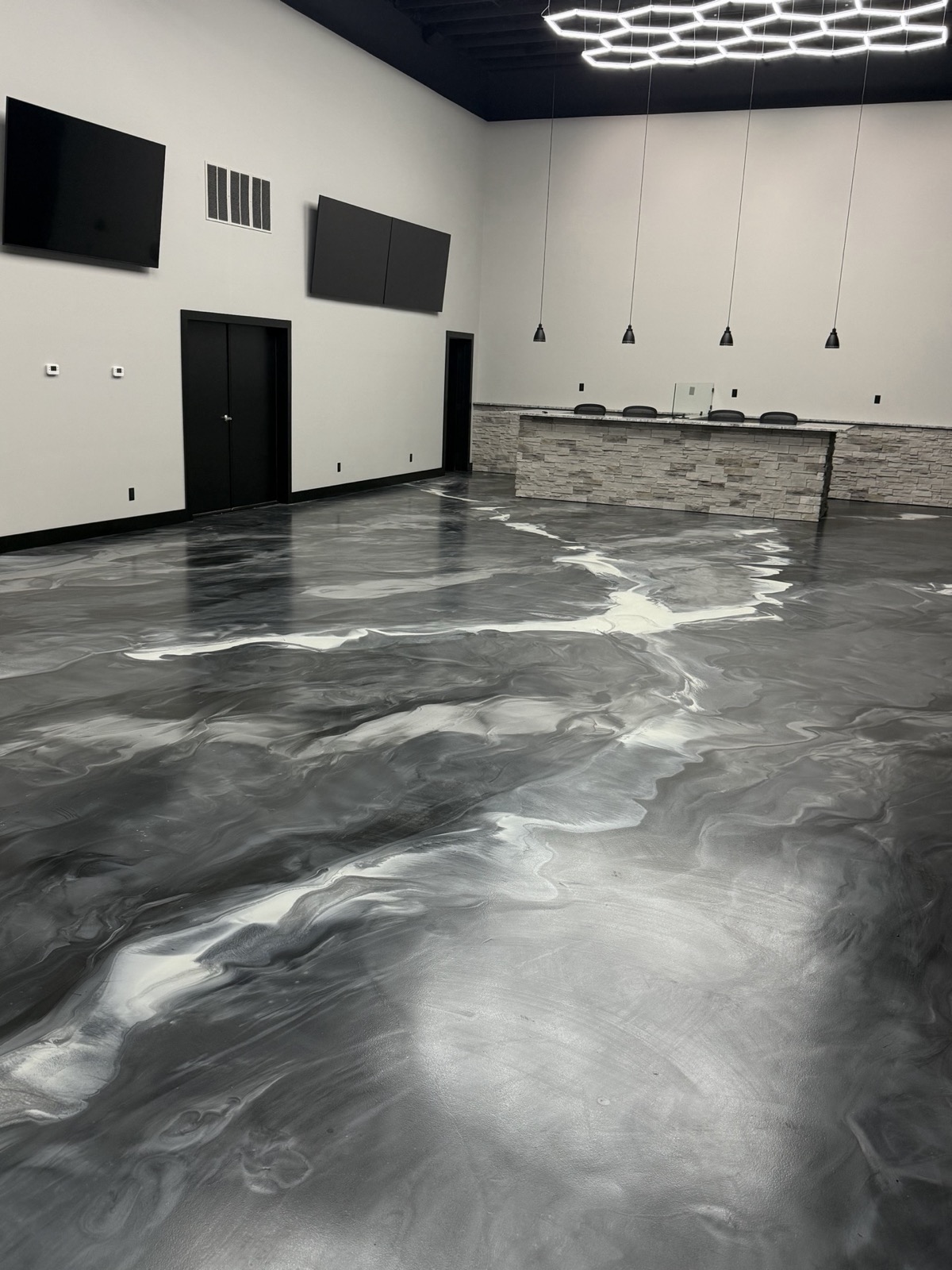 Finished interior with a stone-faced bar, granite countertop, pendant lights, and metallic epoxy floor by Ireland Construction